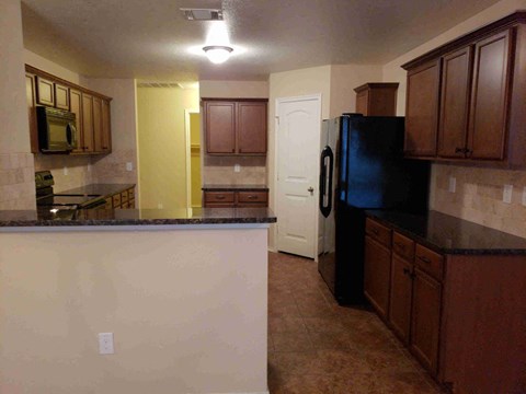 A kitchen with brown cabinets and a black fridge.