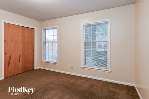 a bedroom with a carpeted floor and a door and two windows