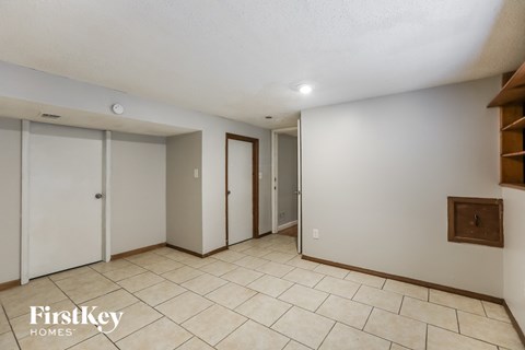 A spacious room with a tile floor and white walls, with a wooden shelf on the right wall.