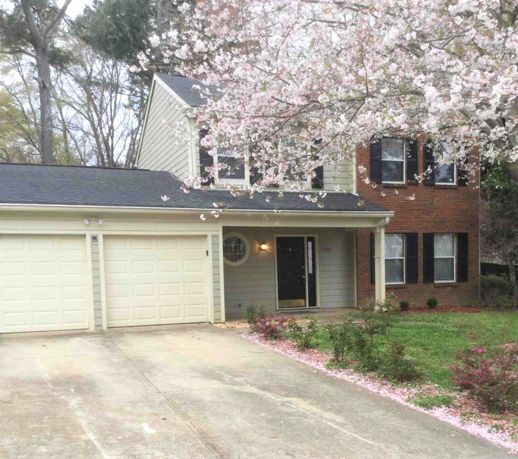 A house with a driveway and a tree with pink flowers in front.