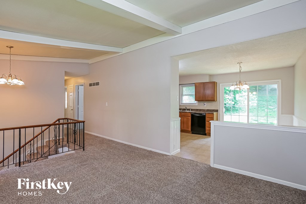 A spacious living room with a staircase and a kitchen in the background.