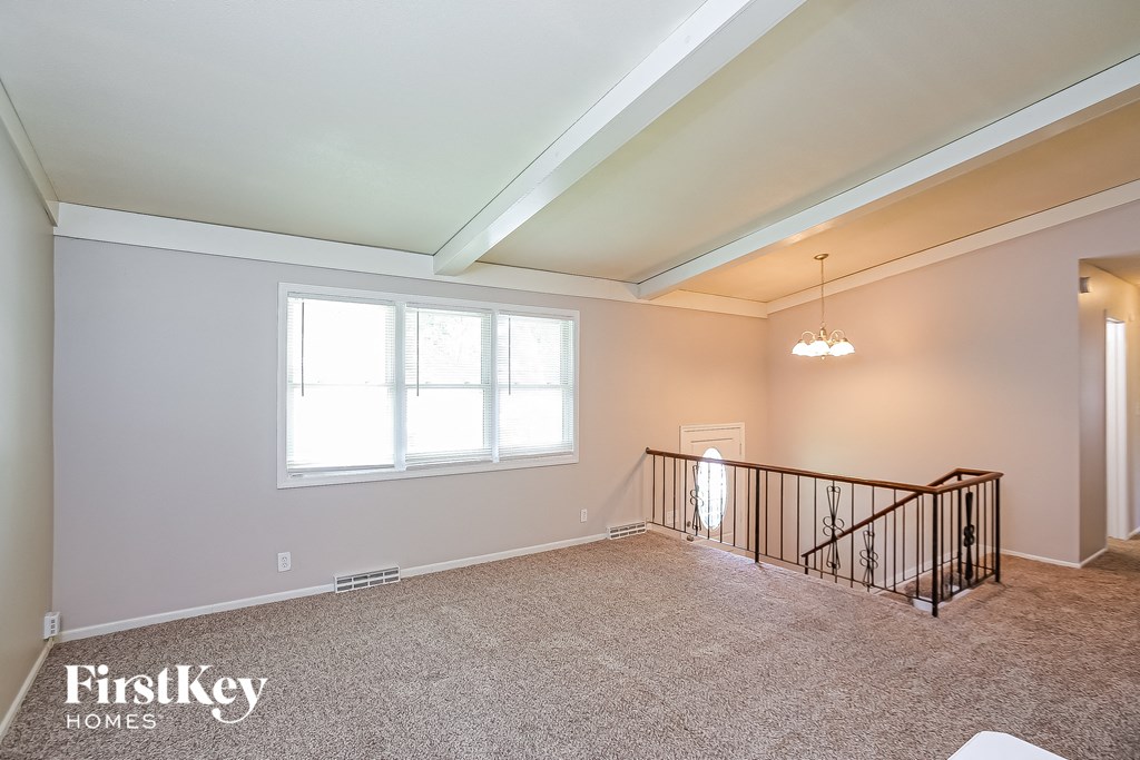 A spacious room with a carpeted floor, a staircase with a metal railing, and a chandelier hanging from the ceiling.