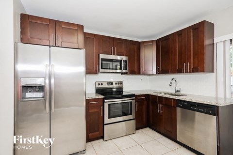 A kitchen with a refrigerator, microwave, oven, and sink.