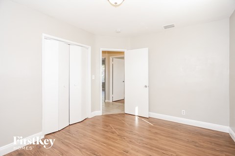 A room with wooden floors and white walls, with a doorway leading to another room.