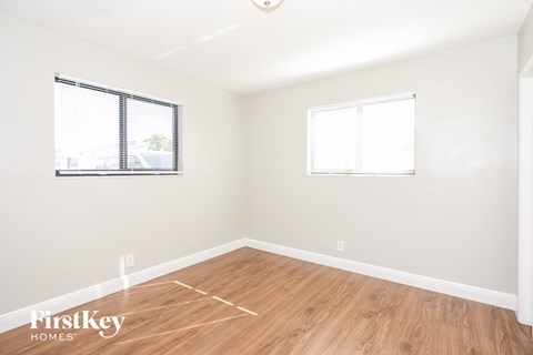 A room with wooden flooring and two windows.