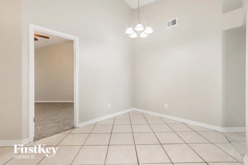 a empty living room with a white tiled floor and a door to a hallway