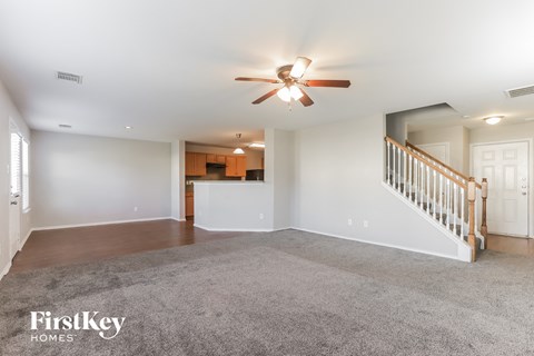 A spacious living room with a ceiling fan and a staircase.