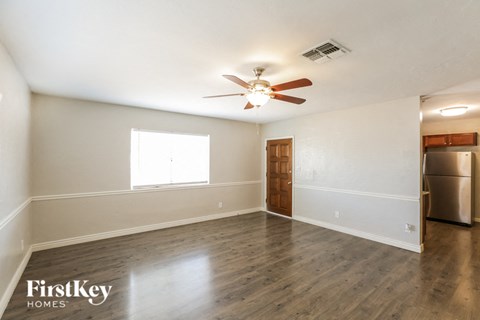 an empty living room with a ceiling fan and a kitchen