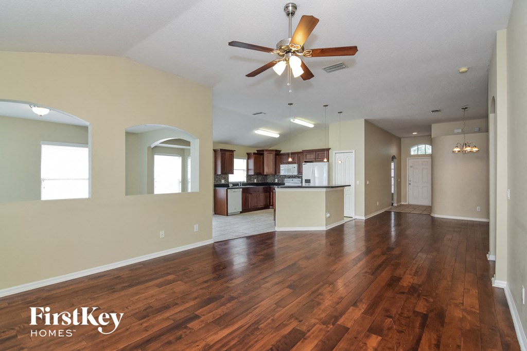 an empty living room with a ceiling fan and a kitchen