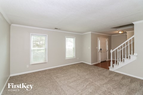 the living room and entryway of a house with carpet and stairs
