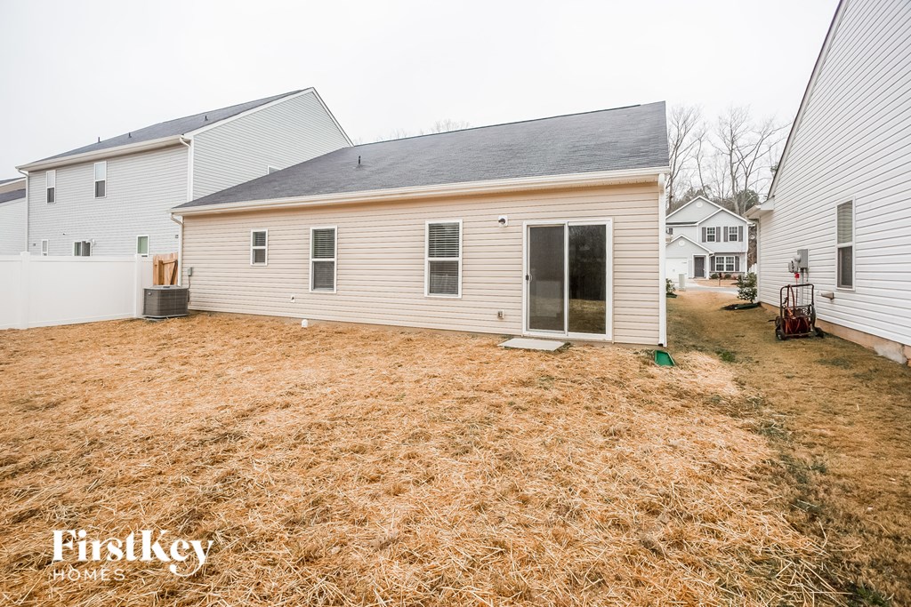 a backyard with a white house and a yard with brown grass