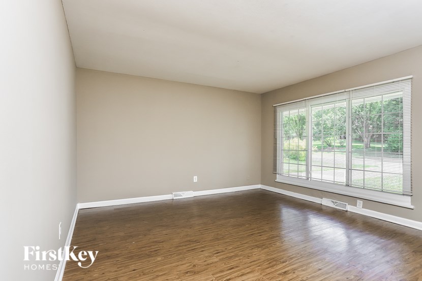 A room with wooden flooring and a large window with blinds.