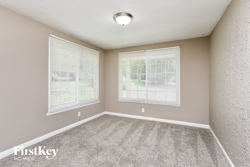 A room with a carpeted floor and two windows with blinds.