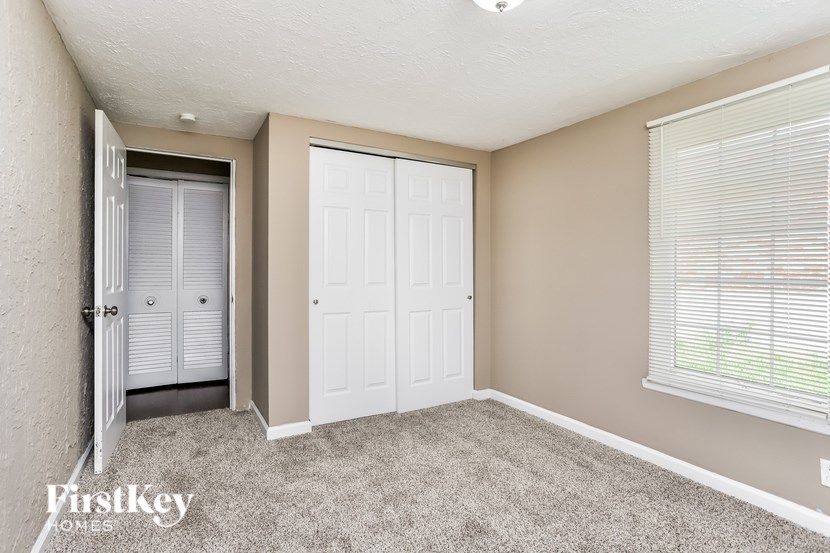 A bedroom with a white door and a grey carpet.