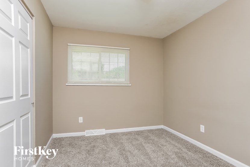 A room with a carpeted floor and a window with blinds.