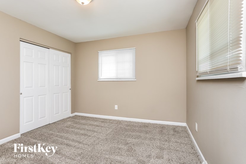 A room with a carpeted floor, a window with blinds, and a door.