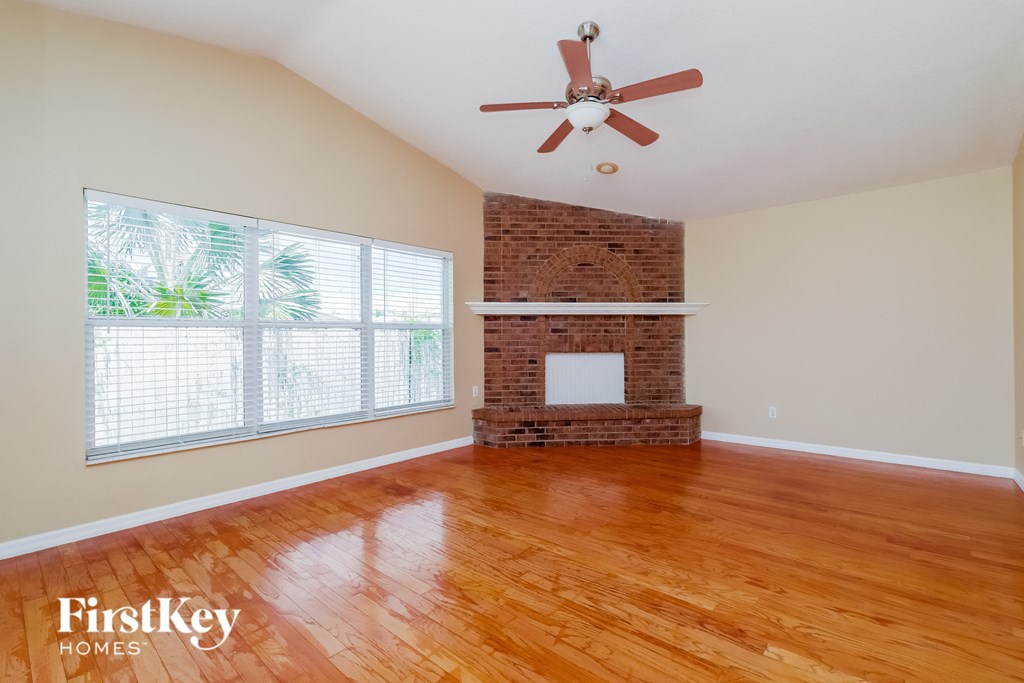 a living room with wood floors and a brick fireplace and a ceiling fan
