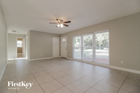 an empty living room with large windows and a ceiling fan