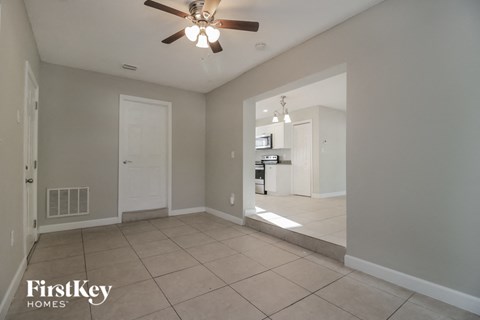 an empty living room with a ceiling fan and a kitchen