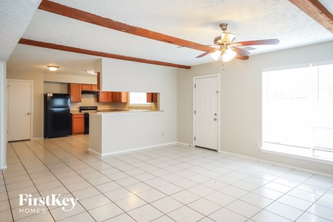 A spacious room with a ceiling fan and a kitchen area in the background.