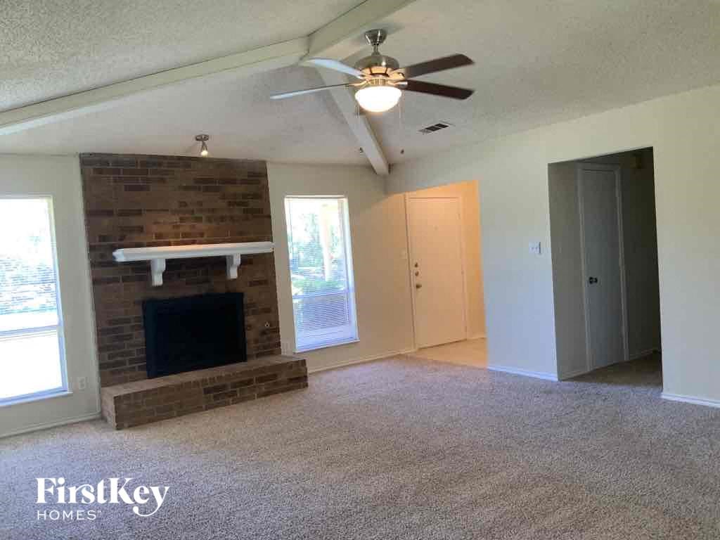 an empty living room with a brick fireplace and a ceiling fan