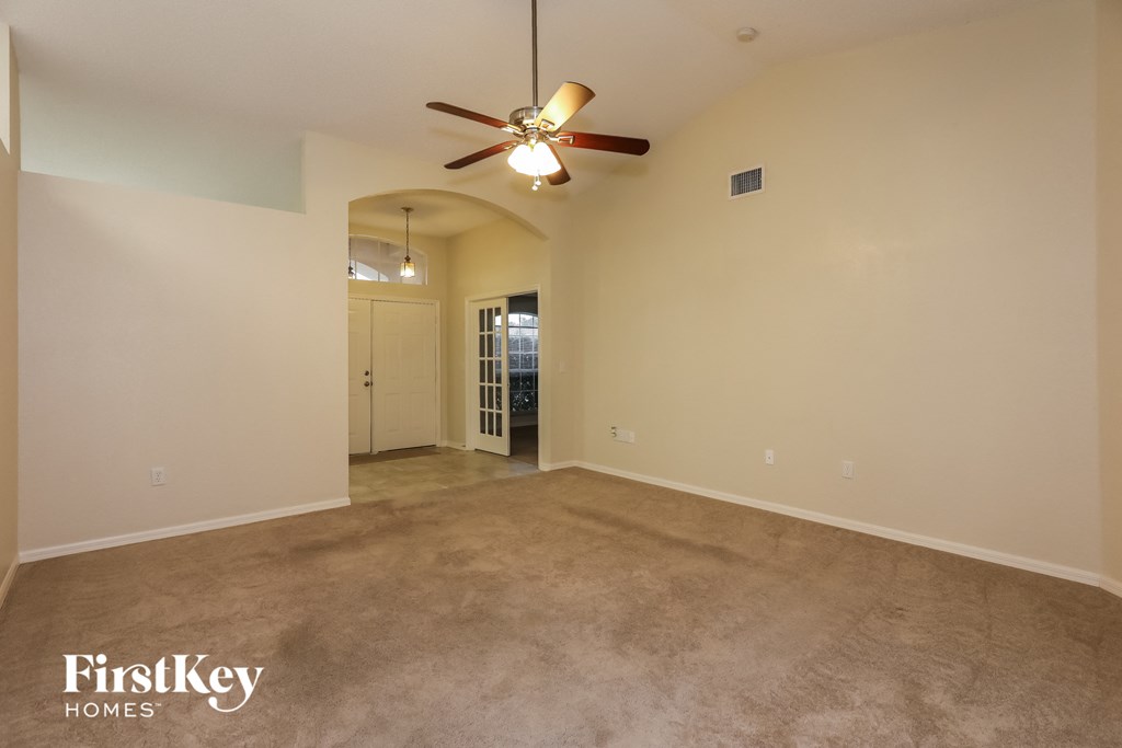 an empty living room with a ceiling fan and a carpet