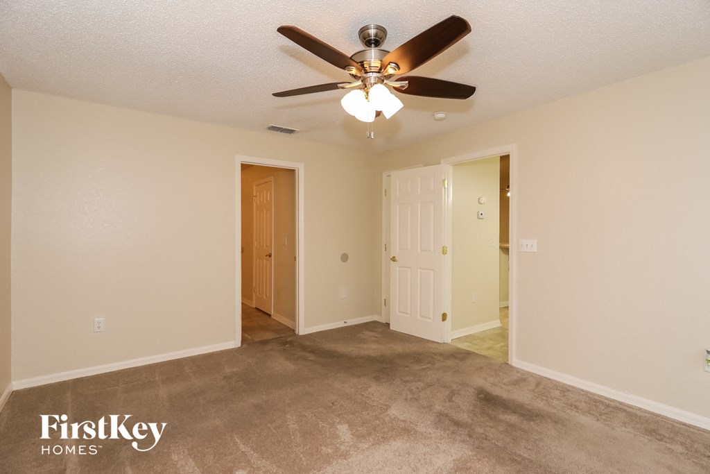 an empty living room with a ceiling fan and a door to a hallway