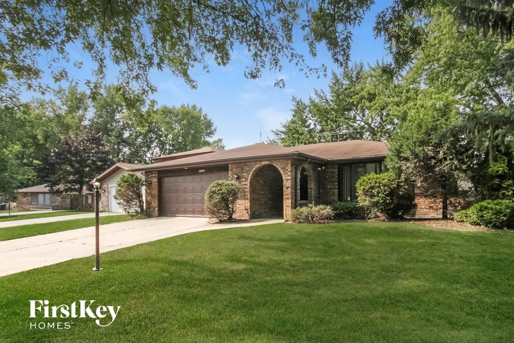 A house with a brown roof and a garage door is surrounded by greenery.