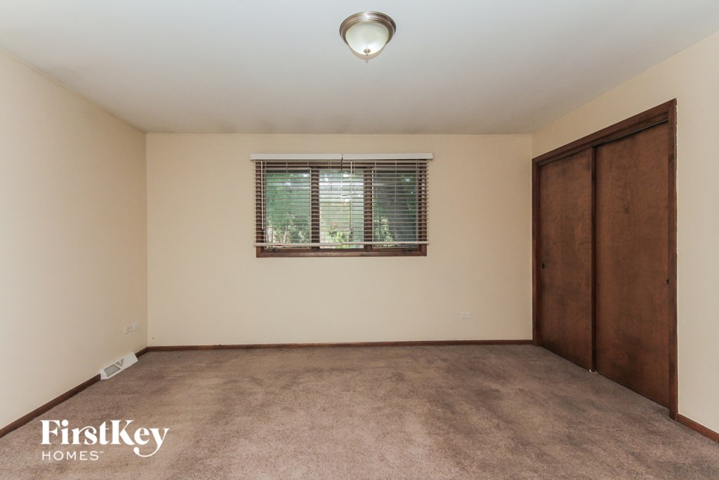 A room with a brown carpet and a window with blinds.