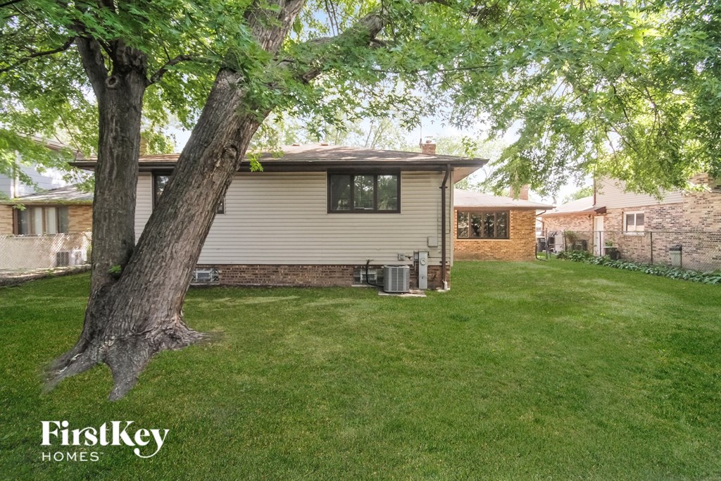 A tree in a yard with a house in the background.