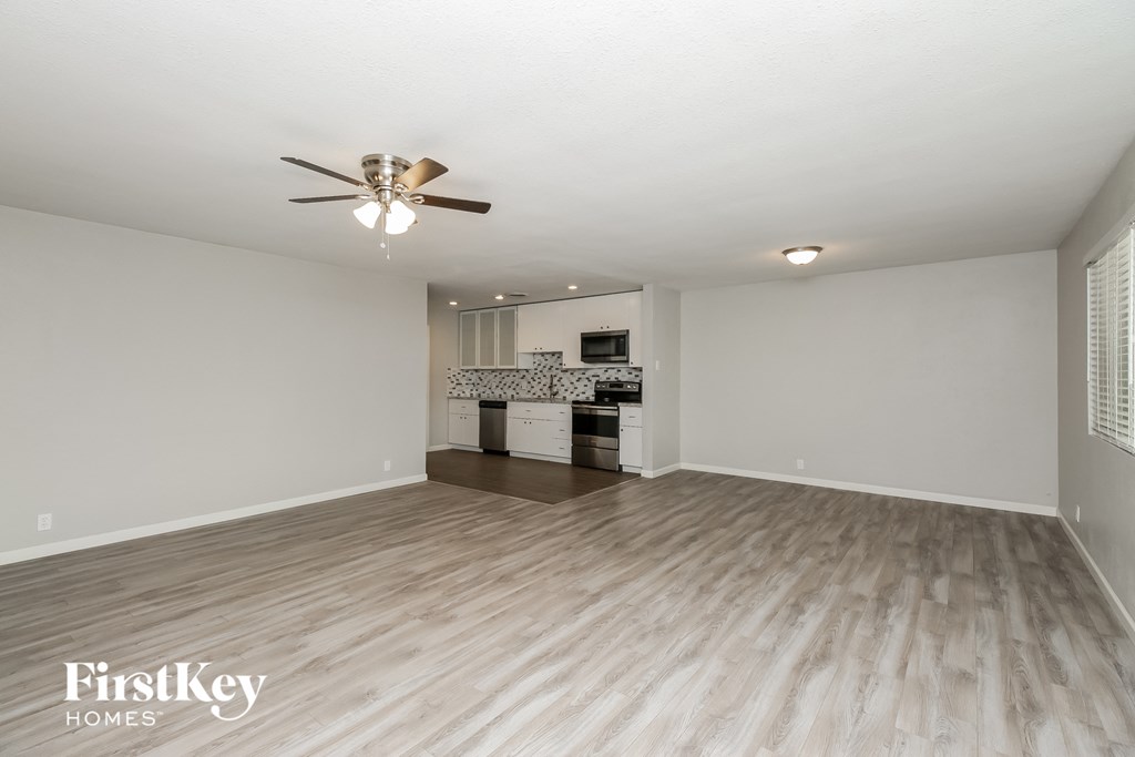 an empty living room with a ceiling fan and a kitchen