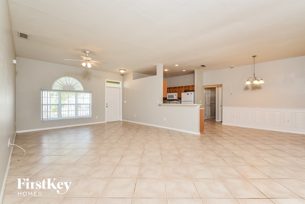 an empty living room with a kitchen in the background