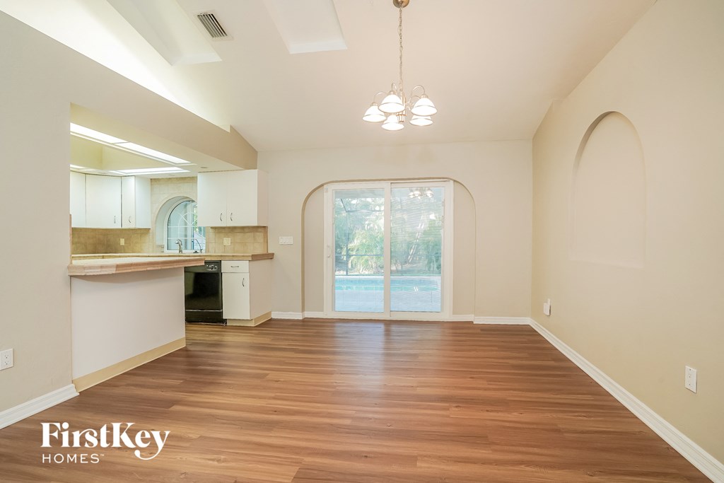 A spacious room with wooden floors and a kitchen area with white cabinets.