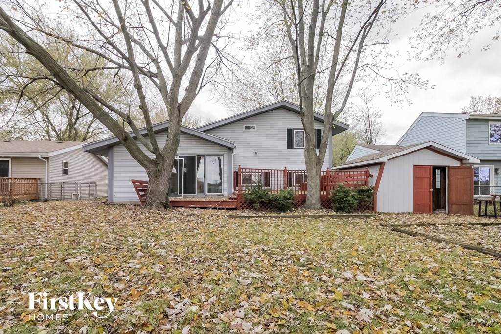 a white house with a yard with trees and a red fence