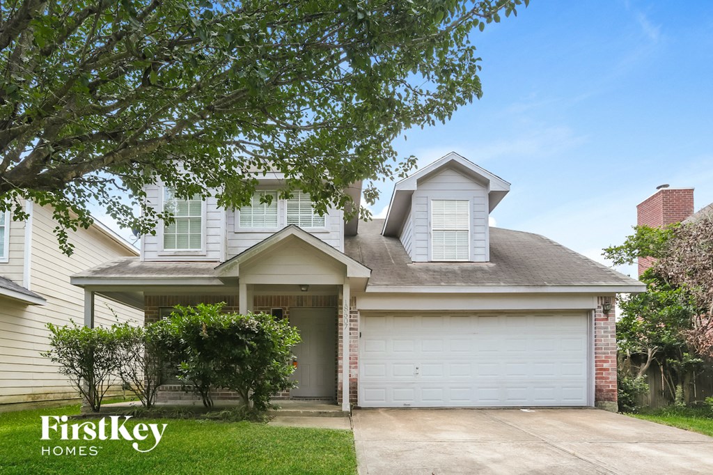 a white house with a garage door and a tree