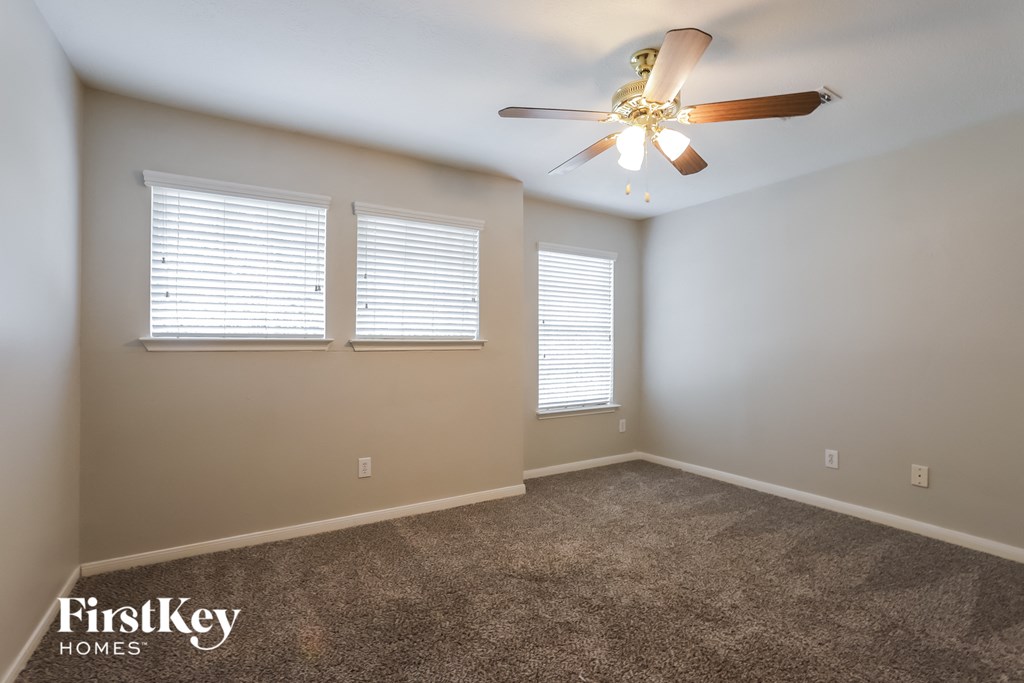 an empty room with a ceiling fan and two windows