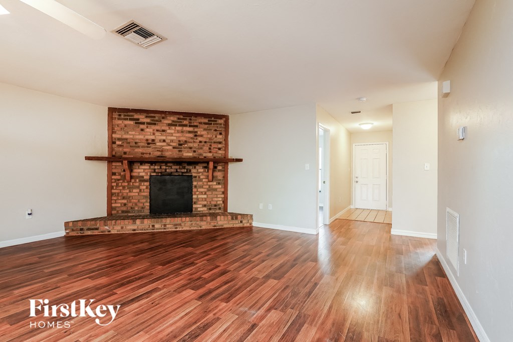 an empty living room with a brick fireplace and wooden floors