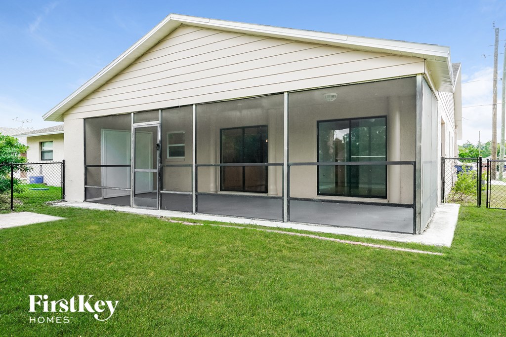 a screened in porch of a white house with a green lawn