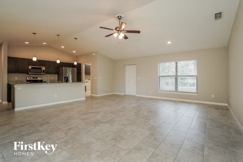 A spacious living room with a kitchen in the background and a ceiling fan.