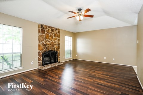 A spacious room with a stone fireplace and wooden flooring.