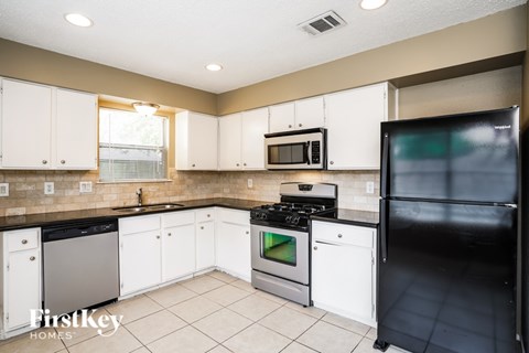 A kitchen with white cabinets and a black fridge.