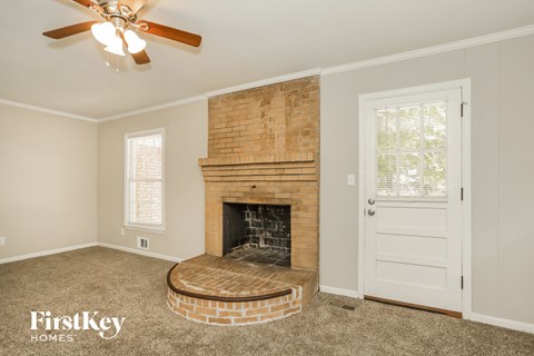 an empty living room with a brick fireplace and a ceiling fan
