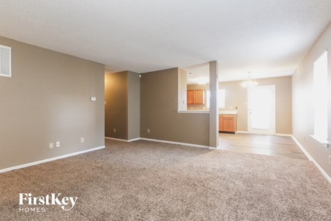 an empty living room with carpet and a kitchen