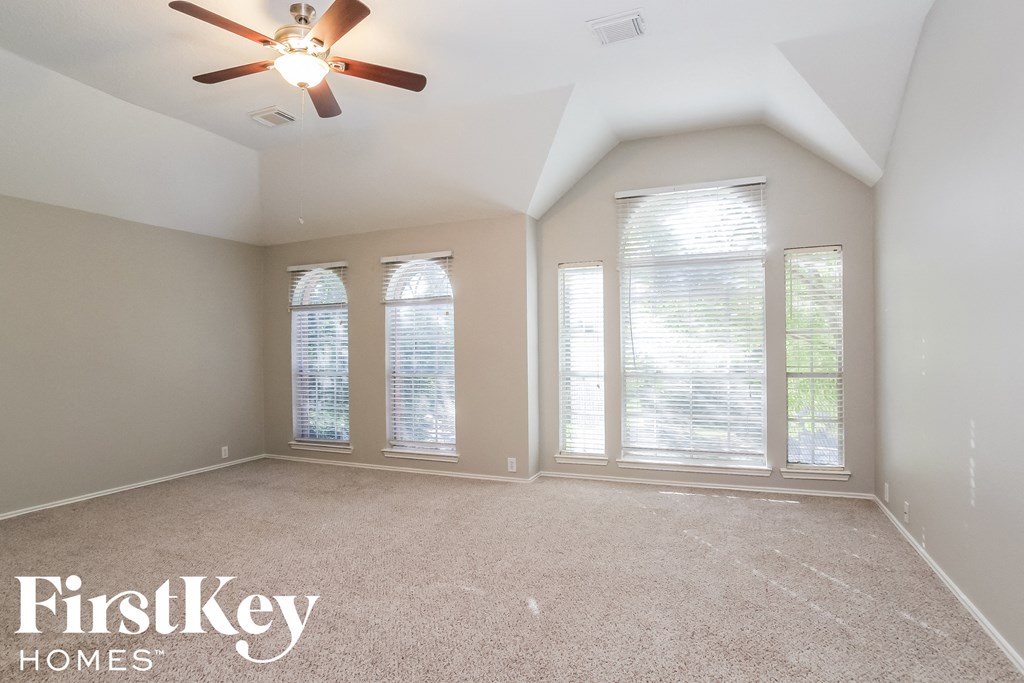 an empty living room with a ceiling fan and three windows