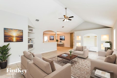 A living room with a beige couch and a painting of a sunset on the wall.