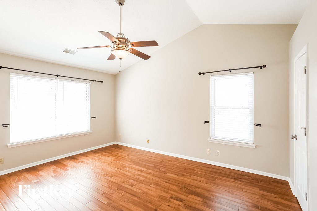 A room with a ceiling fan and two windows.