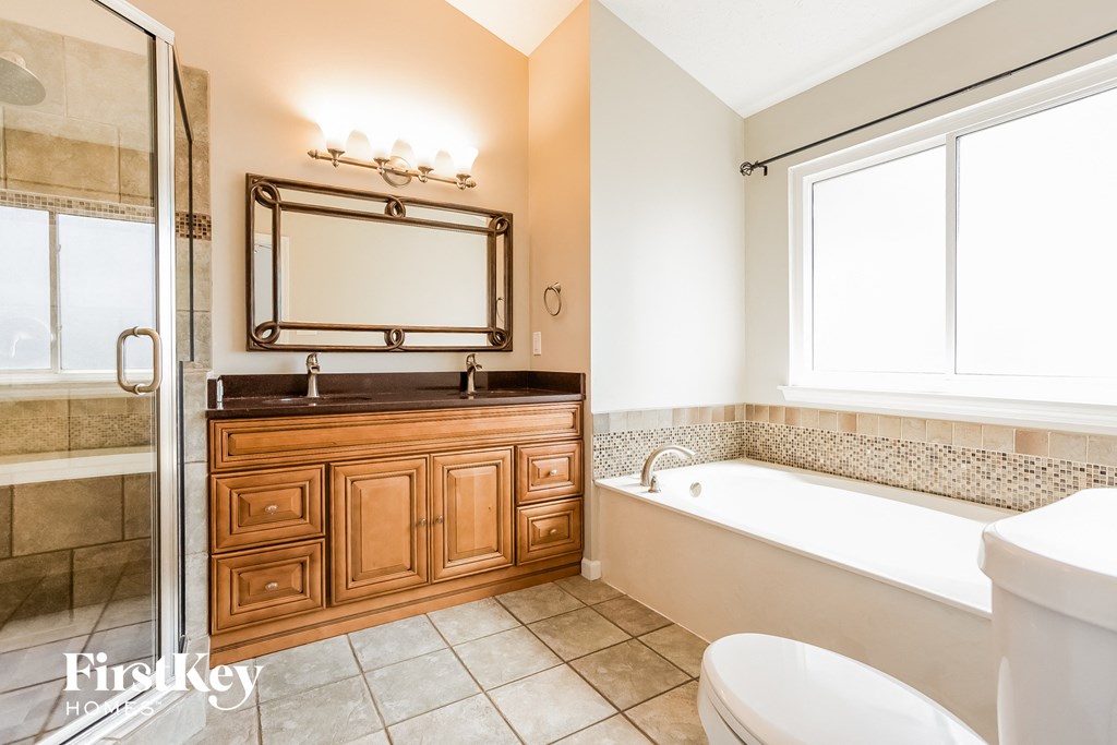 A bathroom with a white tub, wooden vanity, and a large mirror.
