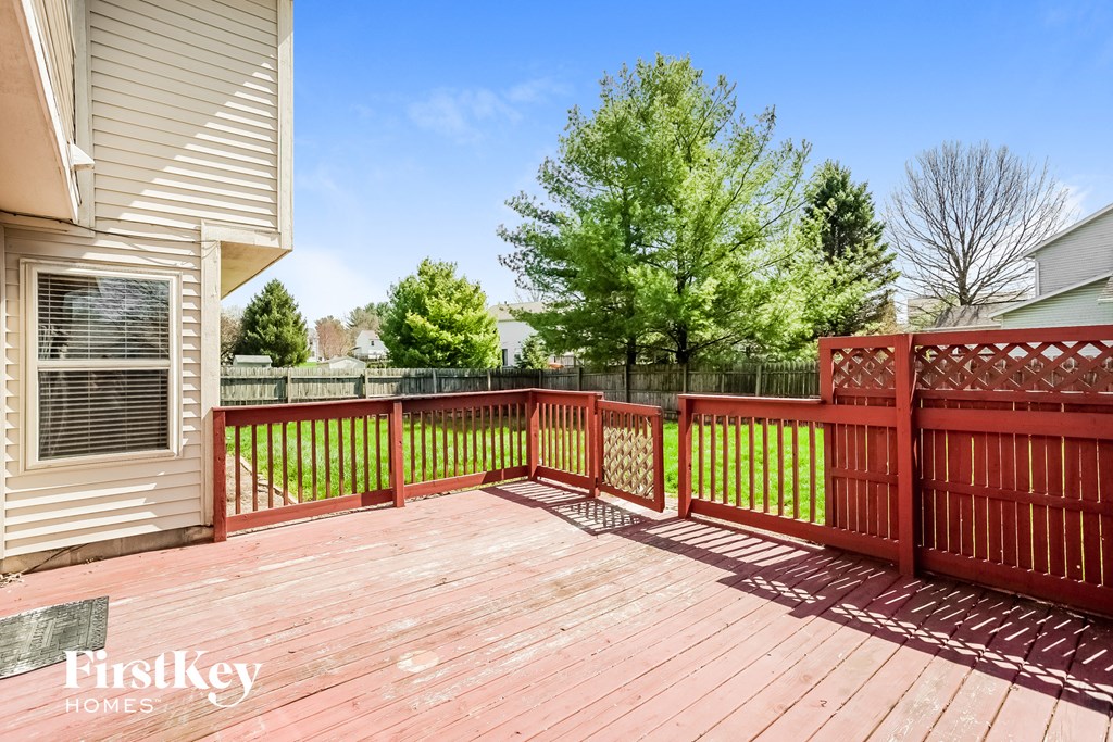 A wooden deck with a red fence and a green mat in front of a house.