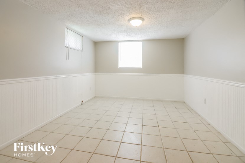 an empty living room with white tile and a window