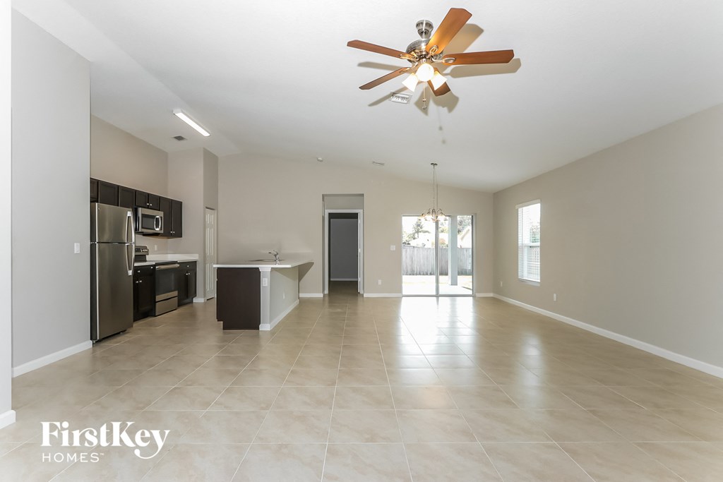 an empty living room and kitchen with stainless steel appliances and a ceiling fan